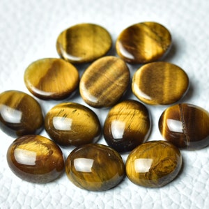 K&ouml;nnte beinhalten: Eine Sammlung von 12 ovalen Tigeraugen-Edelsteinen. Die Steine sind eine Mischung aus goldbraunen und braunen Farben mit einem chatoyanten Effekt.
