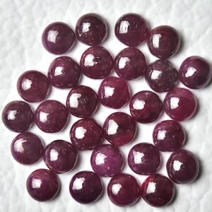 May include: A collection of round, polished ruby gemstones. The rubies are a deep red color and have a smooth, glossy finish.