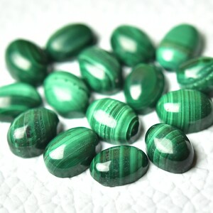 May include: A collection of oval-shaped malachite gemstones, each with a unique green and white striped pattern. The stones are smooth and polished, with a glossy finish.