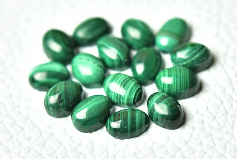May include: A collection of oval-shaped malachite gemstones, each with a unique green and white striped pattern. The stones are smooth and polished, with a glossy finish.
