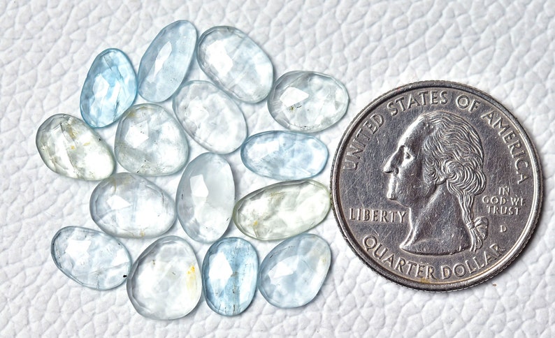 Puede incluir: Una colecci&oacute;n de 17 piedras preciosas de aguamarina azul claro, cada una con forma ovalada facetada. Las piedras est&aacute;n dispuestas en semic&iacute;rculo y tienen aproximadamente el tama&ntilde;o de una moneda de 25 centavos de d&oacute;lar estadounidense.