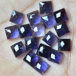 Peut inclure: Une collection de 15 pierres précieuses carrées facettées de couleur violette. Les pierres précieuses sont taillées en forme carrée avec un sommet pointu et ont une couleur violette foncée.