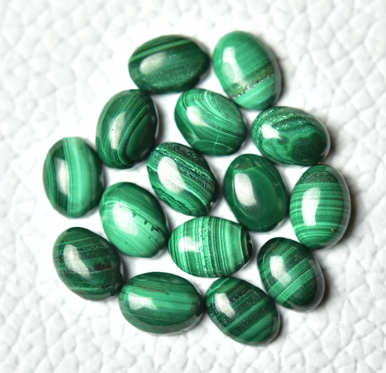 May include: A collection of oval-shaped malachite gemstones, each with a unique green and white pattern. The stones are smooth and polished, with a glossy finish.