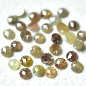 Op de afbeelding: Een verzameling ronde, gefacetteerde, bruine, gele en groene ruwe diamanten. De diamanten zijn verspreid over een wit oppervlak.