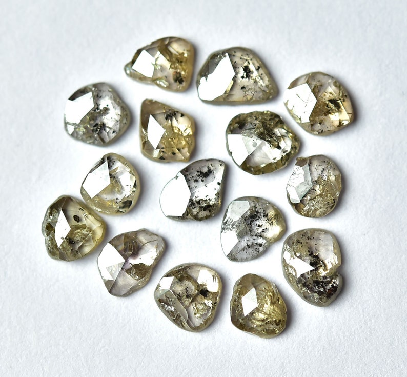 May include: A collection of 14 rough, unpolished, grey and green diamonds. The diamonds are various sizes and shapes, with some having a more rounded shape and others having a more pointed shape.