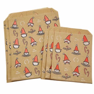 K&ouml;nnte beinhalten: Ein Set aus hellbraunen Papiert&uuml;ten mit einem wiederkehrenden Muster aus Weihnachtsmannfiguren mit roten M&uuml;tzen, Zuckerstangen und Texten wie Naughty or Nice, Joy to All und Ho! Ho! Ho! Die T&uuml;ten weisen eine vertikal gerippte Textur auf.