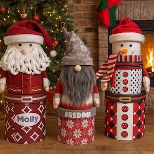 Op de afbeelding: Drie decoratieve dozen met kerstthema. Eén is de kerstman, één is een kabouter genaamd Freddie en de andere is een sneeuwpop. De Santa-doos is rood met de naam "Molly". De sneeuwpop heeft een rood-witte sjaal.