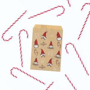 K&ouml;nnte beinhalten: Eine rechteckige braune Papiert&uuml;te mit einem wiederkehrenden Muster aus kleinen Gnomen mit roten M&uuml;tzen und wei&szlig;en B&auml;rten, durchsetzt mit Zuckerstangen. Mehrere rot-wei&szlig; gestreifte Zuckerstangen sind um die Papiert&uuml;te herum verstreut.