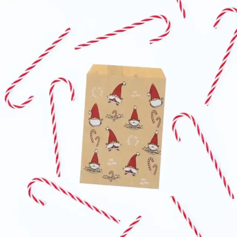 K&ouml;nnte beinhalten: Eine rechteckige braune Papiert&uuml;te mit einem wiederkehrenden Muster aus kleinen Gnomen mit roten M&uuml;tzen und wei&szlig;en B&auml;rten, durchsetzt mit Zuckerstangen. Mehrere rot-wei&szlig; gestreifte Zuckerstangen sind um die Papiert&uuml;te herum verstreut.
