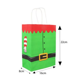 May include: A green paper gift bag with a red top and white handles. The bag is designed to look like an elf's outfit, with a belt, buttons, and an arm with a striped sleeve. The bag measures 8cm wide, 16cm long, and 22cm tall.