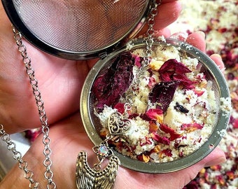 May include: A silver tea infuser with a chain and a decorative angel wing charm. The infuser is filled with dried rose petals and white powder.