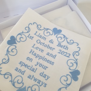 May include: White embroidered fabric with blue cursive lettering and hearts. The text reads "Liam & Beth 1st October 2022 Love and Happiness on your special day and always".