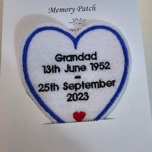 May include: A heart-shaped Memory Patch with a blue border and the word "Grandad" and dates embroidered in black. A small red heart is at the bottom. The patch is on a white background with the words "Memory Patch" at the top.