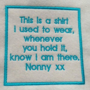 May include: A white fabric square with a blue embroidered border. The text inside the border reads: "This is a shirt I used to wear, whenever you hold it, know I am there. Nonny xx"