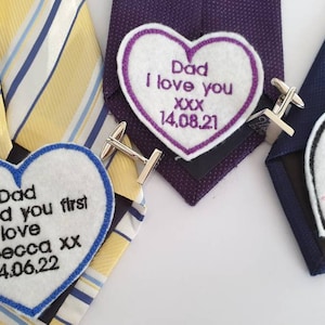 May include: Three heart-shaped tie tacks with embroidered messages. The first tack is blue with the text "Dad I loved you first love Rebecca xx 14.06.22". The second tack is purple with the text "Dad I love you xxx 14.08.21". The third tack is black with the text "Love you xxx".