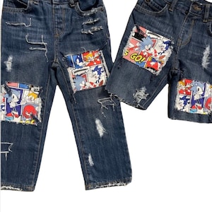 May include: Two pairs of blue denim jeans with patches of a Sonic the Hedgehog comic book print. The jeans are distressed with rips and tears.