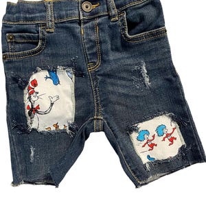May include: Distressed denim shorts with patches featuring illustrations from the book "The Cat in the Hat". The patches show the Cat in the Hat, Thing 1, and Thing 2.