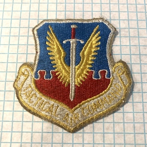 May include: Embroidered patch with a blue, red, and gold design. The patch features a sword, wings, and the text "TACTICAL AIR COMMAND". The patch has a gold border.