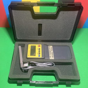 May include: A black plastic case with a gray foam interior holds a yellow and gray electronic device. The device has a small screen and several buttons. A gray probe and cable are also inside the case. Text on the device reads "ESC 1000".