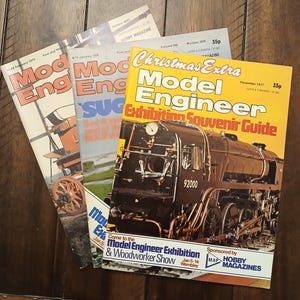 May include: Three vintage Model Engineer hobby magazines from the late 1970s. The top issue features a large black steam locomotive on a yellow cover with the text Christmas Extra Model Engineer Exhibition Souvenir Guide and MAP Hobby Magazines.