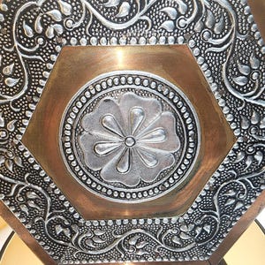 May include: A hexagonal metal tray featuring a central silver-toned flower motif surrounded by a smooth copper-colored border. The outer frame is decorated with intricate silver-toned embossed floral patterns and a textured stippled background.