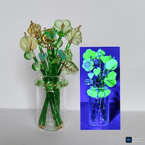 May include: A small glass vase containing a handcrafted glass flower arrangement. The flowers are made of green, gold, and clear glass beads and leaf shapes. The vase is clear, and the stems are green. A smaller image shows the flowers glowing.