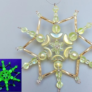 以下が含まれることがあります： 複雑なデザインの手作り雪の結晶オーナメント。中央の花の形と放射状のアームが特徴で、すべて虹色のビーズと金色の金属棒で作られています。このオーナメントは繊細で華やかな外観で、ホリデーデコレーションに最適です。
