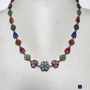 May include: A necklace featuring a series of multi-colored beads shaped like flowers and leaves, connected by thin bronze-toned metal links. The beads include shades of blue, green, orange, red, and purple, arranged in a symmetrical pattern.