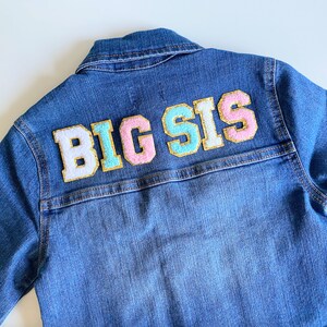 May include: A blue denim jacket with a white, pink, and light blue felt patch that says "BIG SIS" on the back.