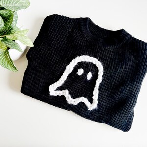 Puede incluir: Su&eacute;ter de punto negro con un dise&ntilde;o de fantasma blanco tejido a crochet.