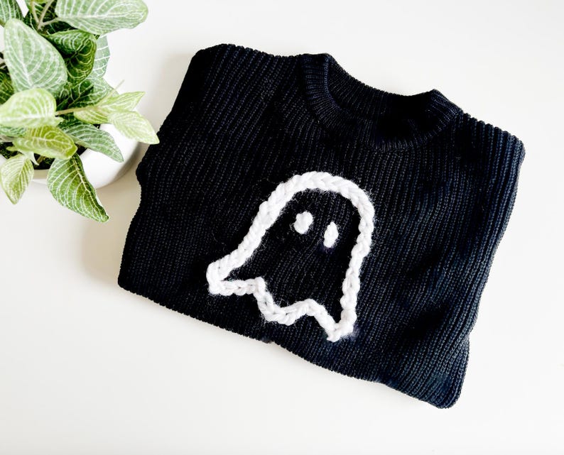 Puede incluir: Su&eacute;ter de punto negro con un dise&ntilde;o de fantasma blanco tejido a crochet.