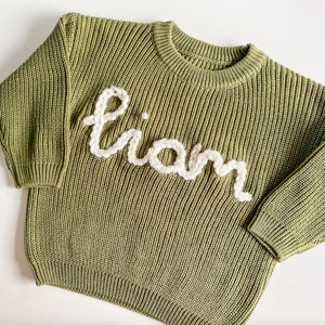 May include: A green knitted sweater with the name "Liam" embroidered in white yarn.