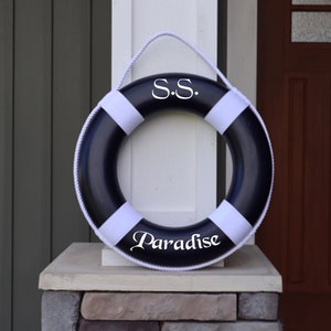 May include: A black and white life preserver with the text "S.S. Paradise" written on it.