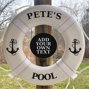 May include: White life preserver with black text that reads "PETE'S" and "POOL". The life ring has two black anchor graphics and a black circle in the center with the text "ADD YOUR OWN TEXT". White rope is attached.
