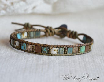 May include: A brown leather bracelet with a row of turquoise, white, and brown square beads. The bracelet has a leather tie closure.