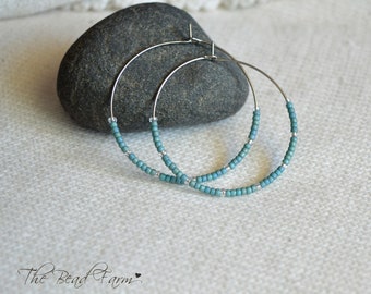 May include: A pair of silver hoop earrings with turquoise and silver beads. The earrings are on a gray rock.