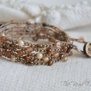 May include: A multi-strand bracelet made with brown cord and beige, brown, and clear beads. The bracelet has a brown button closure.