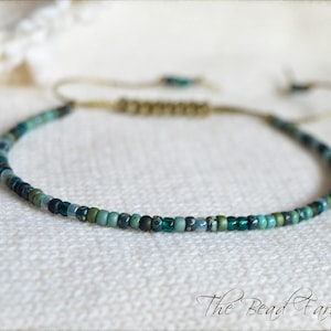 May include: A delicate green and blue beaded necklace with a sliding knot closure. The necklace is made with small, round beads and has a subtle ombre effect.