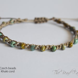 May include: Handmade macrame bracelet featuring a series of green and brown Czech beads. The beads are strung on a khaki-colored cord, creating a delicate and earthy design. The bracelet is adjustable and suitable for various wrist sizes.