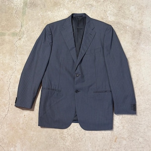 May include: A dark gray blazer featuring a subtle vertical pinstripe pattern, a notched lapel, two black front buttons, and four smaller black buttons on each sleeve cuff. The garment includes a chest pocket and two lower flap pockets.