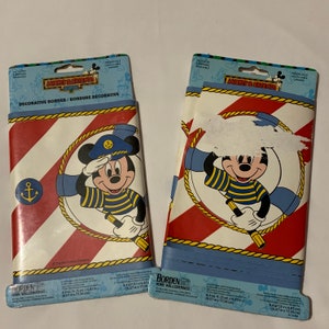 May include: Two rolls of Mickey Mouse themed wallpaper border. The border features a red and white striped pattern with a blue and white life preserver with Mickey Mouse dressed as a sailor. The text on the packaging reads "Mickey & Friends" and "Decorative Border/Bordure Décorative".