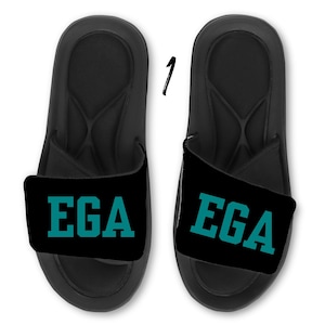 May include: Pair of black slides with adjustable straps. The straps are teal blue and have the text "EGA" printed in white.