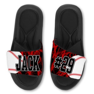 May include: Black slide sandals with a red and black lightning bolt pattern and a white baseball with red stitching. The strap has the name "JACK" and the number "#29" printed on it.