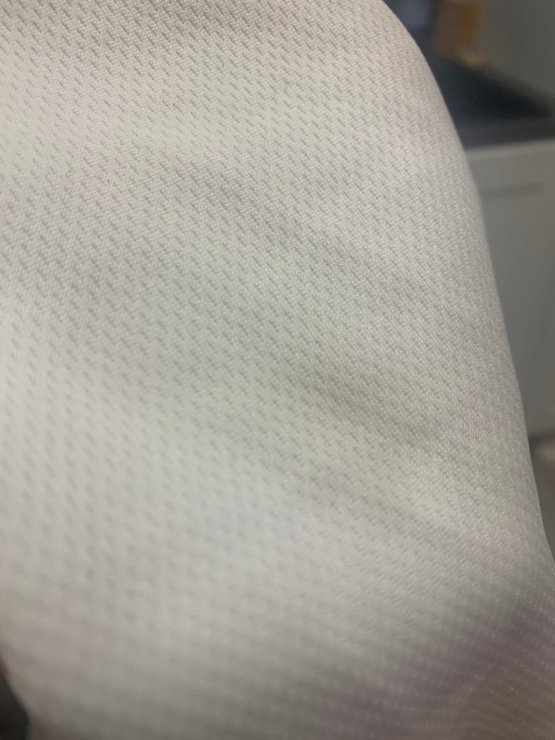 May include: Close-up of a white fabric with a textured pattern. The fabric has a subtle diagonal weave.