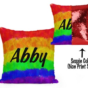 May include: A rainbow-colored pillow with the name "Abby" printed in black on the front. The back of the pillow is red sequins.