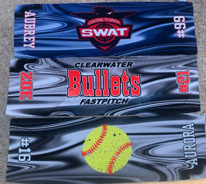 May include: Three softball team banners with black and white wavy designs. The top banner is blue with the text "CENTRAL FLORIDA SWAT" and the number "66#." The middle banner is gray with the text "CLEARWATER Bullets FASTPITCH" and the number "#21." The bottom banner is gray with a yellow softball and the text "AURORA #16."