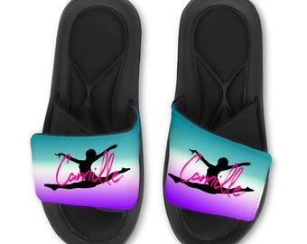 May include: A pair of black slides with a teal, white, and purple ombre design. The slides feature a silhouette of a gymnast in a split and the name "Camille" in pink script.