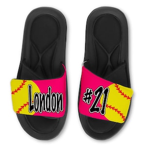 May include: A pair of black slide sandals with a pink and yellow softball design. The left sandal has the name "London" and the right sandal has the number "#21".