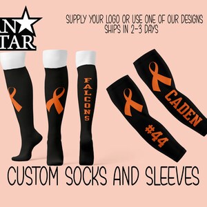May include: Customizable black knee-high socks and arm sleeves with an orange ribbon design. The socks have the word "FALCONS" printed on one side. The sleeves have an orange ribbon and the text "CADEN #44" printed on them.