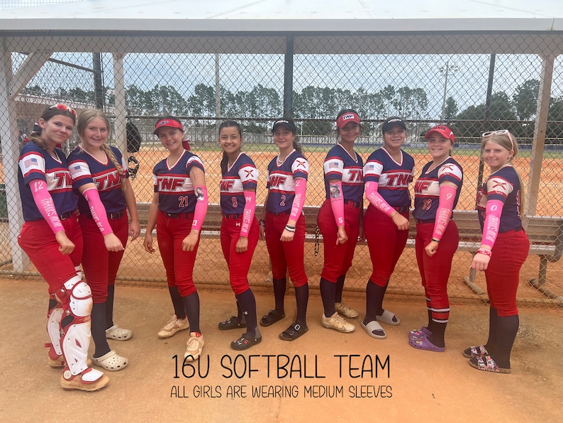 Puede incluir: Un equipo de j&oacute;venes en uniformes de softbol a juego. Los uniformes son azul marino y rojo, con mangas rosas. El texto "16U SOFTBALL TEAM" y "ALL GIRLS ARE WEARING MEDIUM SLEEVES" es visible.